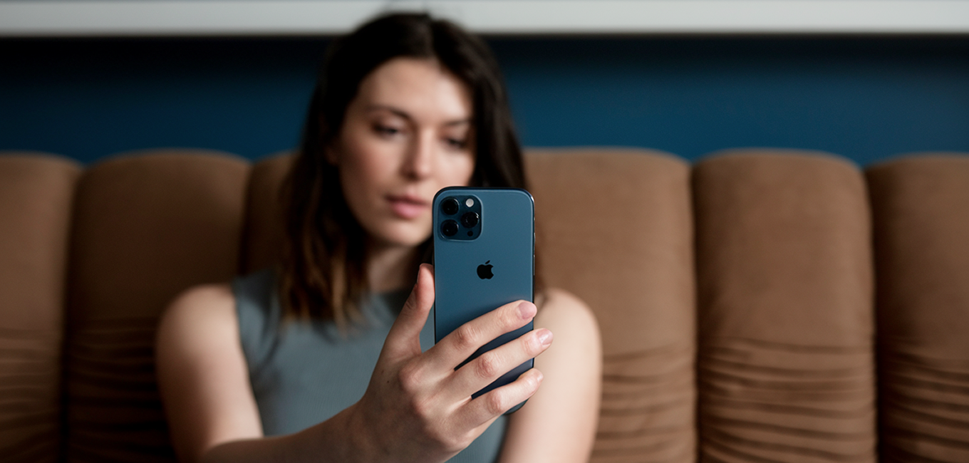 Person sitting on a couch holding a smartphone and looking at the screen.