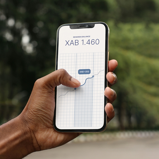 A hand holds a smartphone displaying a chart for a crypto reward balance of XAB 1.460 on a white grid, with a finger touching the rising graph.