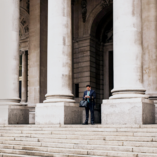 A woman in a light blue jumpsuit sits comfortably in an orange chair, smiling as she uses her smartphone.