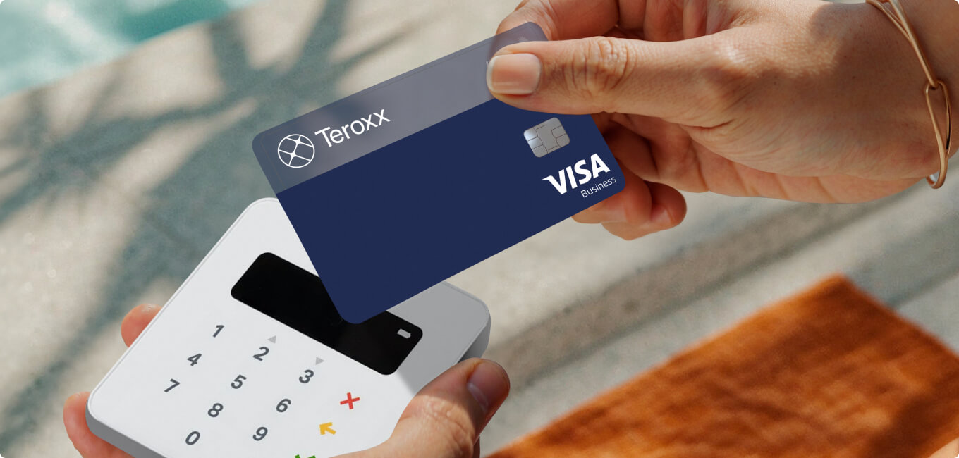 Person holding a blue Teroxx Visa card above a white payment terminal, ready to make a contactless payment outdoors near a pool or sunlit area. Person holding a blue Teroxx Visa card above a white payment terminal, ready to make a contactless payment outdoors near a pool or sunlit area.